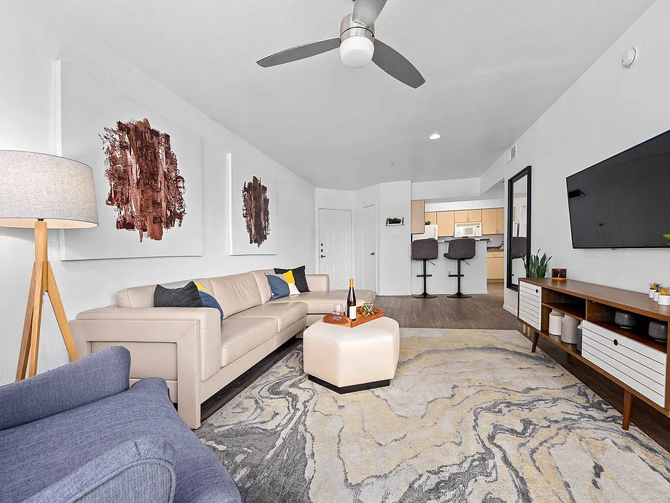 Living room with beige sectional, ceiling fan and wall-mounted TV on hardwood floors