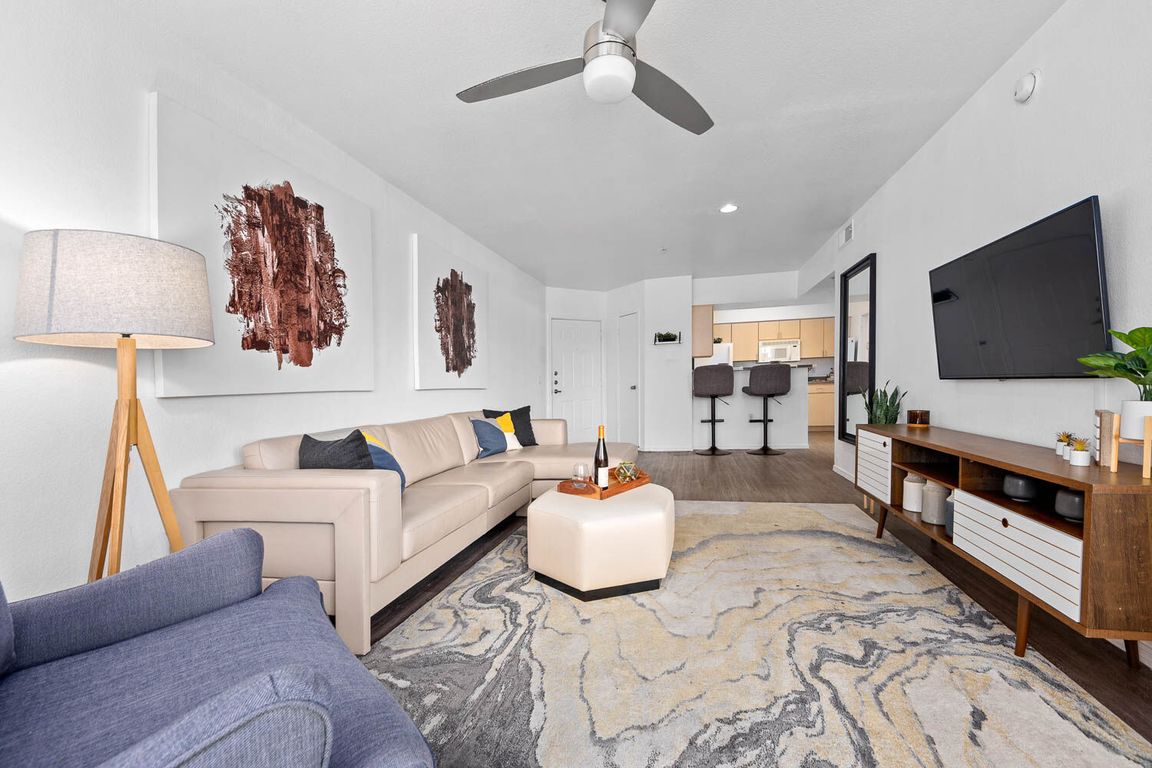 Living room with beige sectional, ceiling fan and wall-mounted TV on hardwood floors
