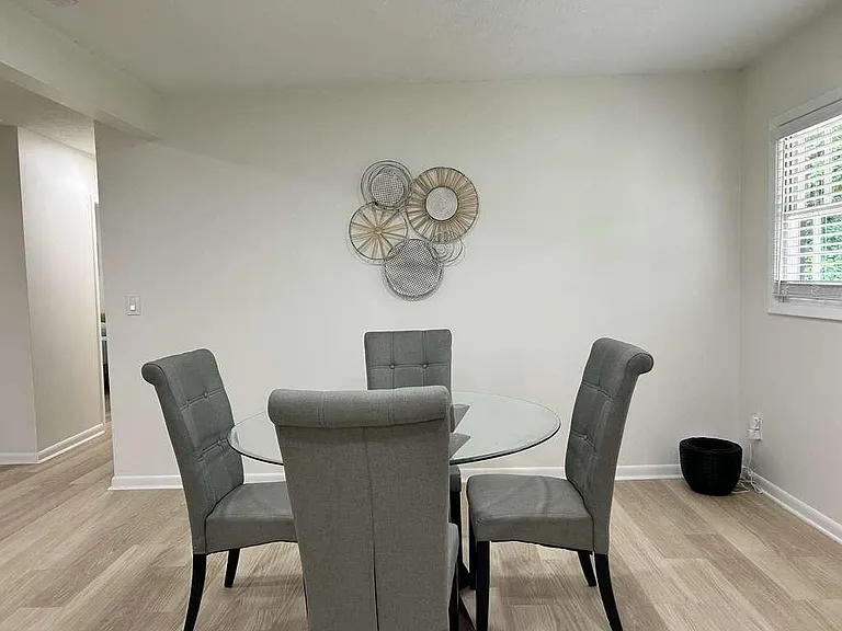 Dedicated dining area with a round glass table, seating for four, and a nearby window with blinds for natural light.