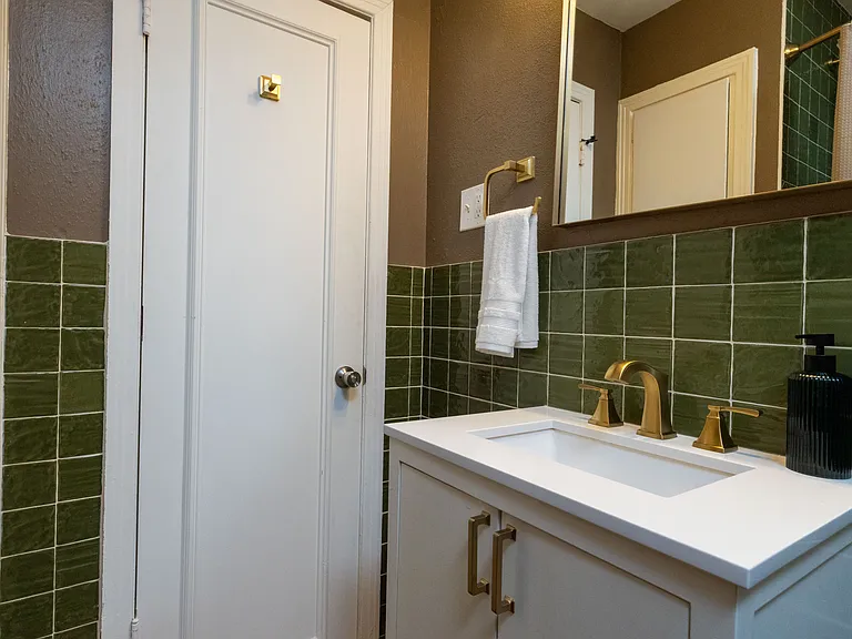 Stylish bathroom with rich green tile, gold accents, and a modern vanity. Enjoy a relaxing soak in the deep tub surrounded by elegant finishes _ a spa-like retreat with timeless charm.