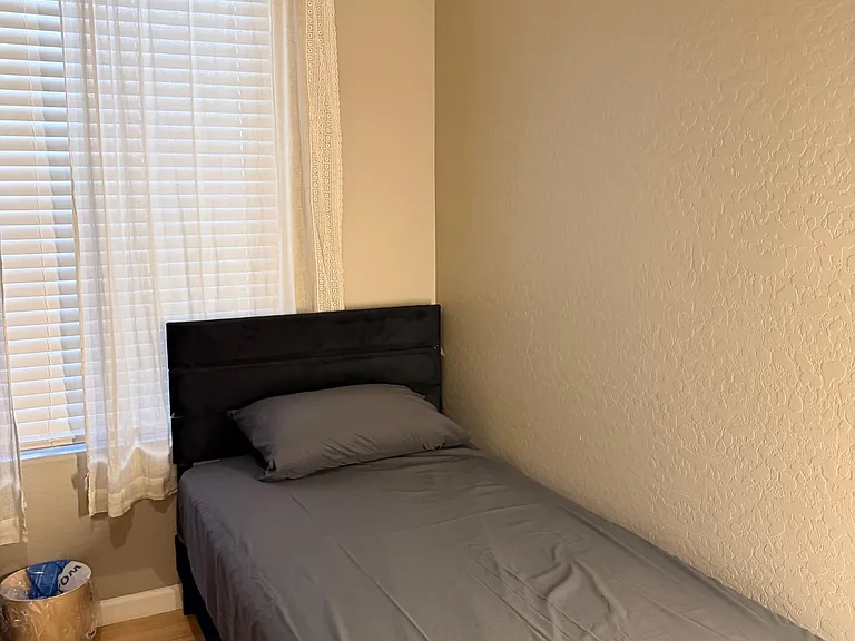 Private bedroom with a furnished bed, window with blinds and curtains, and durable wood-look flooring for easy upkeep.