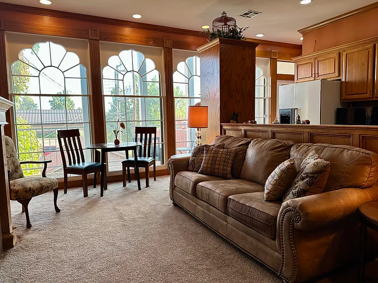 Sun-filled main living area with warm woodwork, sweeping arched windows, and views of the balcony and garden.