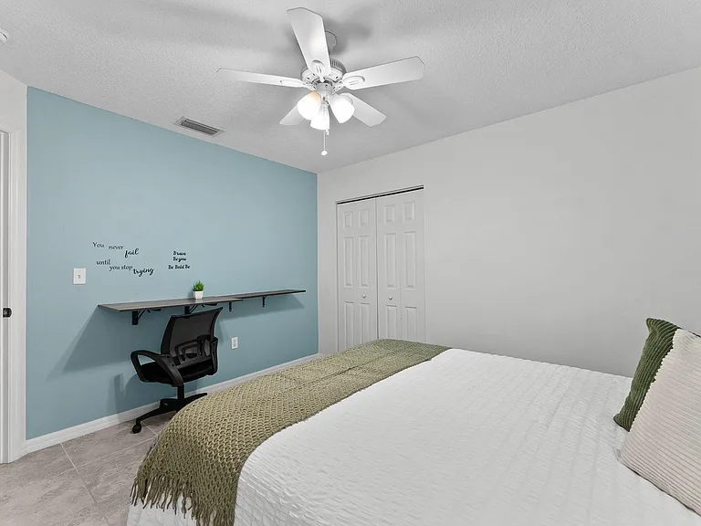 Private bedroom featuring a ceiling fan with light, spacious closet, and a built-in desk/shelf workspace area.