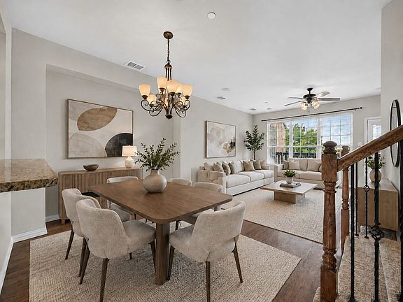 Open-concept living area with wood-finish flooring, a traditional chandelier, a ceiling fan, and a wood staircase with wrought iron balusters