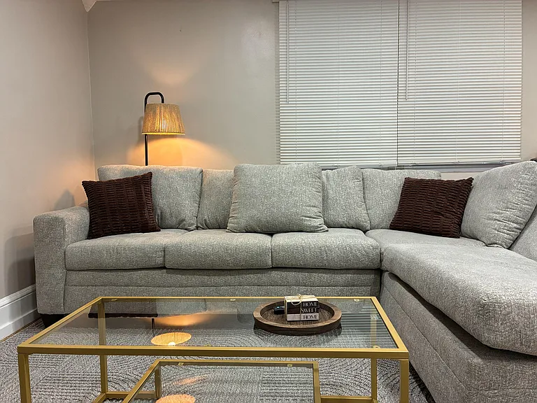 Comfortable living room with a sectional sofa, floor lamp lighting, and a large window with blinds for privacy.