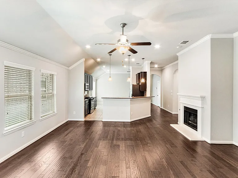 Open-concept living space featuring wood-finish flooring, a white mantel fireplace, and a kitchen island with pendant lighting