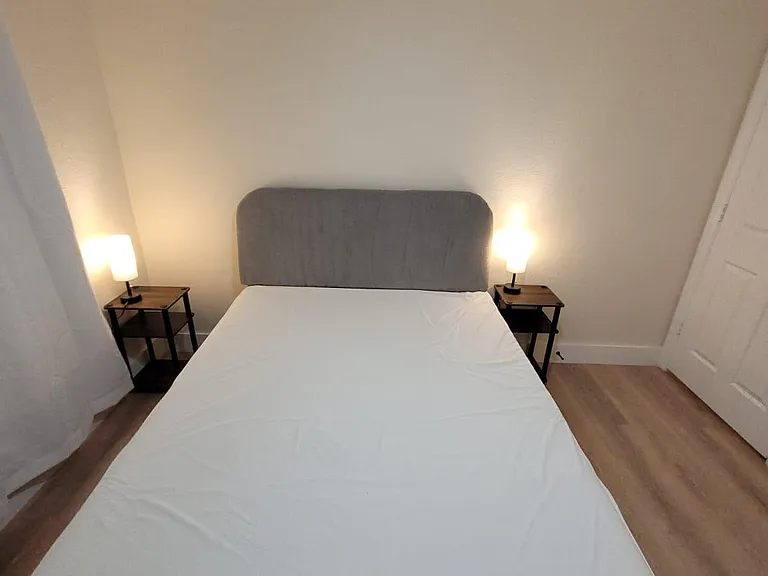 Private bedroom with a full-size bed, upholstered headboard, matching nightstands, and bedside lamps on wood-look flooring.