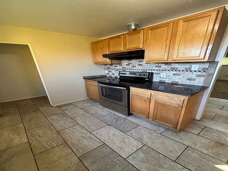 Charming kitchen with modern stainless steel appliances, elegant wooden cabinetry, and stylish stone tile flooring.