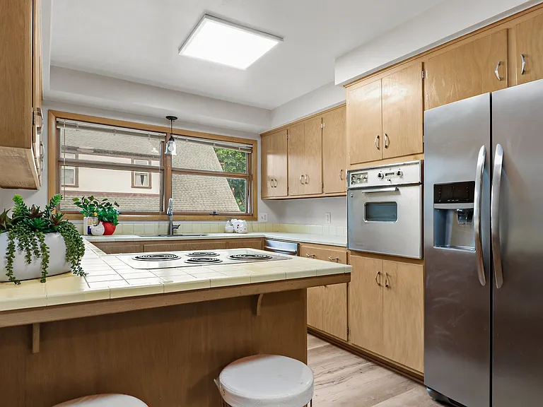 Well lit kitchen. Photographer standing in the space that could have another table, work space, crafting space -- or just more open room!