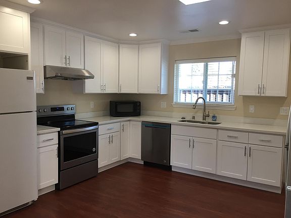 large eat-in kitchen with skylight, quartz countertop, refrigerator, electrical range, range hood, dish washer, and garbage disposal