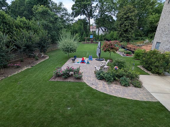 Spacious back yard with playset, additional paver patio, raised beds, and mature blueberry bushes.