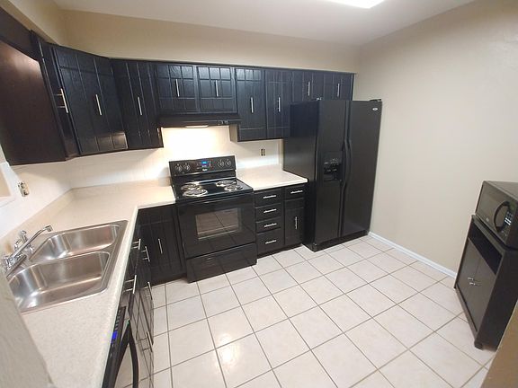 Kitchen has tile floors, black appliance package (fridge, dishwasher, range/oven, microwave, hood that vents outside), black painted cabinets, disposal and new window that looks onto deck/backyard.