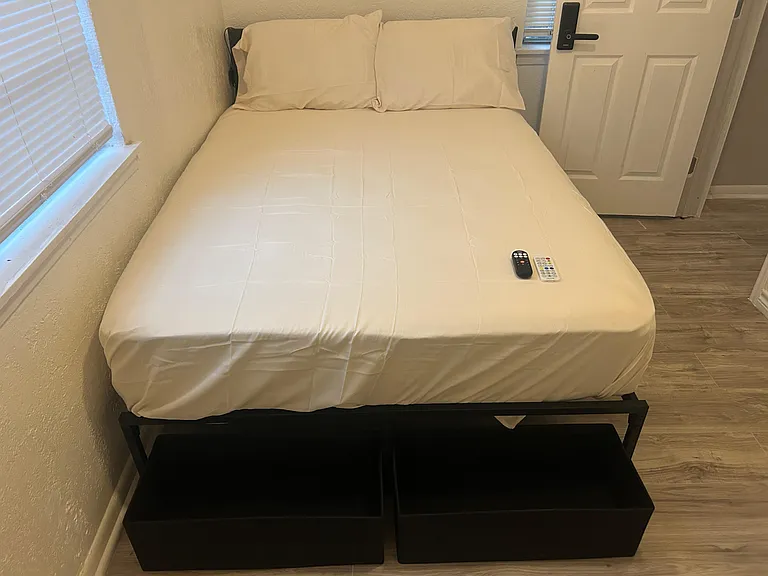 Furnished bedroom featuring a full bed, easy-care flooring, and nearby windows with blinds for light and privacy.