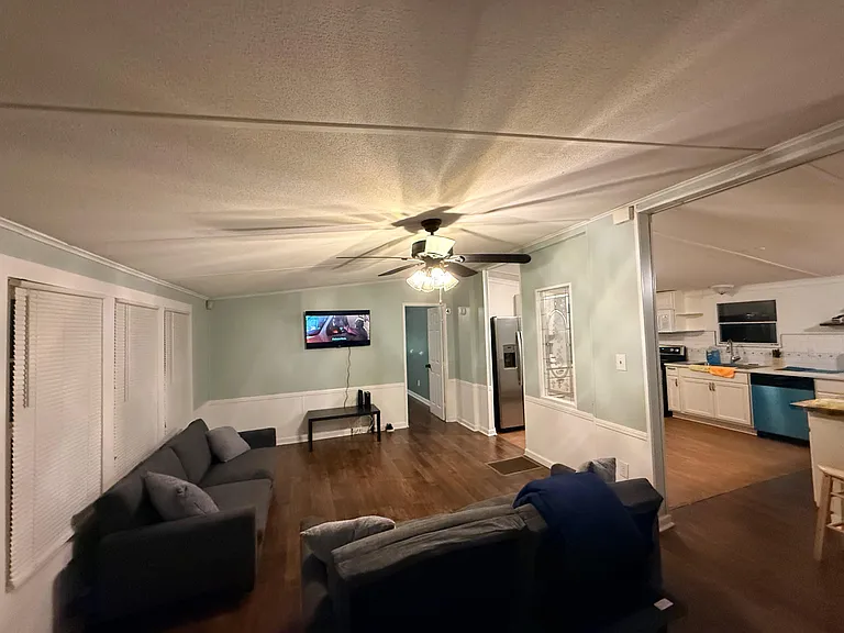 Open living area with wood-style floors, ample seating, and a ceiling fan, flowing into the adjacent kitchen.