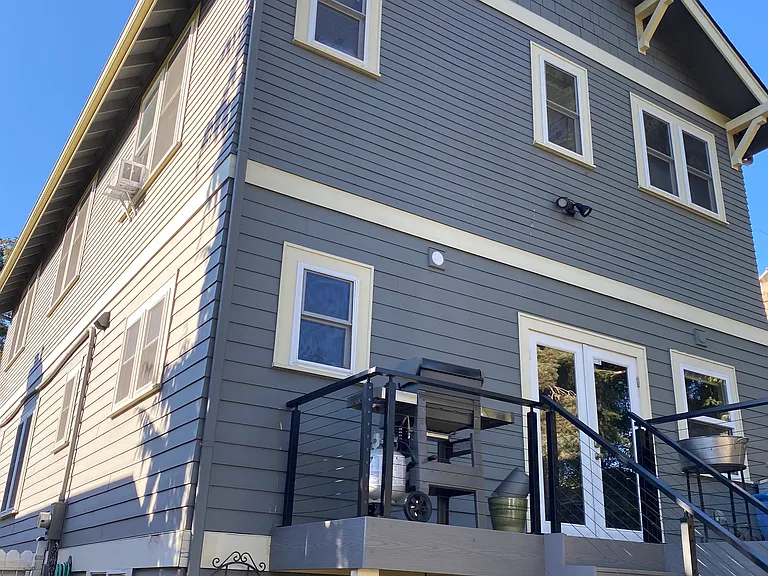 Back of home with BBQ, French doors open to kitchen, deck table seats 4, stairs down to hot tub and fenced yard. Door to lower level opens to TV room.