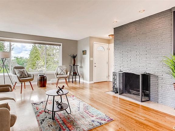 Open concept floor plan with spacious living room  with hardwood floors, sunny wall of western facing windows and wood burning fireplace.  