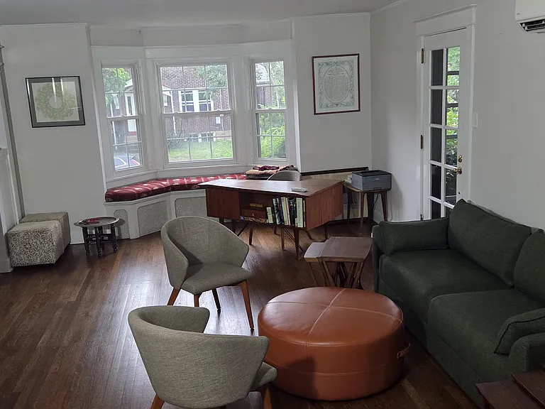 First floor reading room facing south. There is a bay window with a window seat cushion. The dining room and front door are to the left. The door on the right goes to the tiled covered porch.