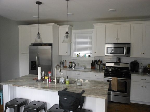 Kitchen features white shaker cabinets, marble counters, and