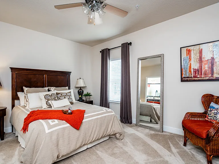 Furnished model bedroom with window, ceiling fan and carpet flooring