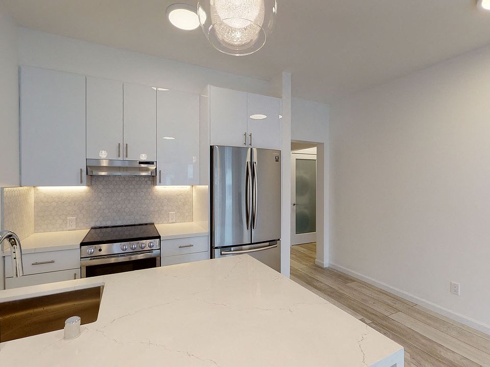 Kitchen with multiple cabinets, refrigerator, stove, range hood, and sink