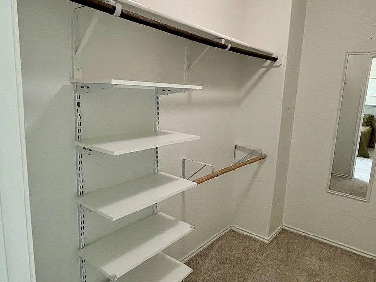 Spacious walk-in closet with built-in shelving and dual hanging rods, offering ample storage and easy organization.