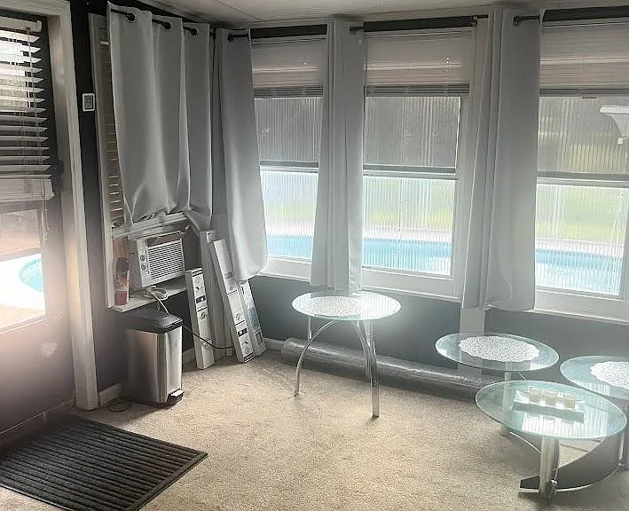 Sunroom-style sitting area with wraparound windows, carpeted floors, and space for cafe seating overlooking the yard.
