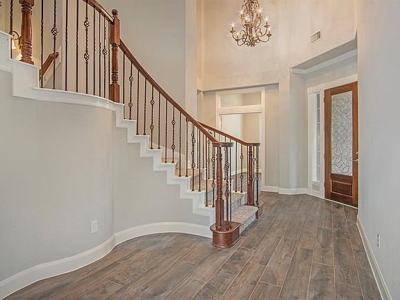 Stunning front entry features leaded glass front door, soaring ceiling with lovely light fixture, wood-look tile floor and a fabulous split staircase with wrought iron spindles.