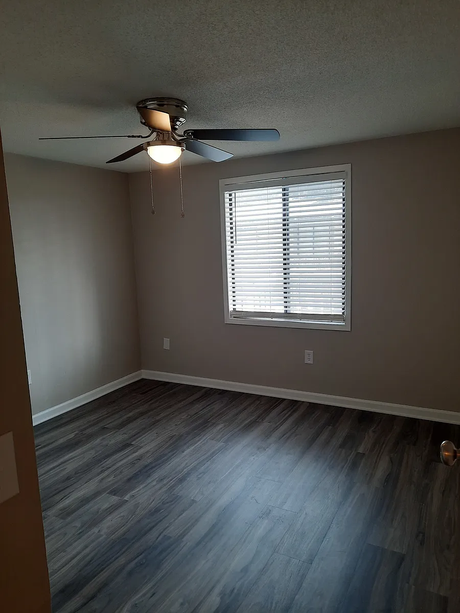 1 bedroom living room with large front window and VCT flooring in light gray - Ridgewood Apartments