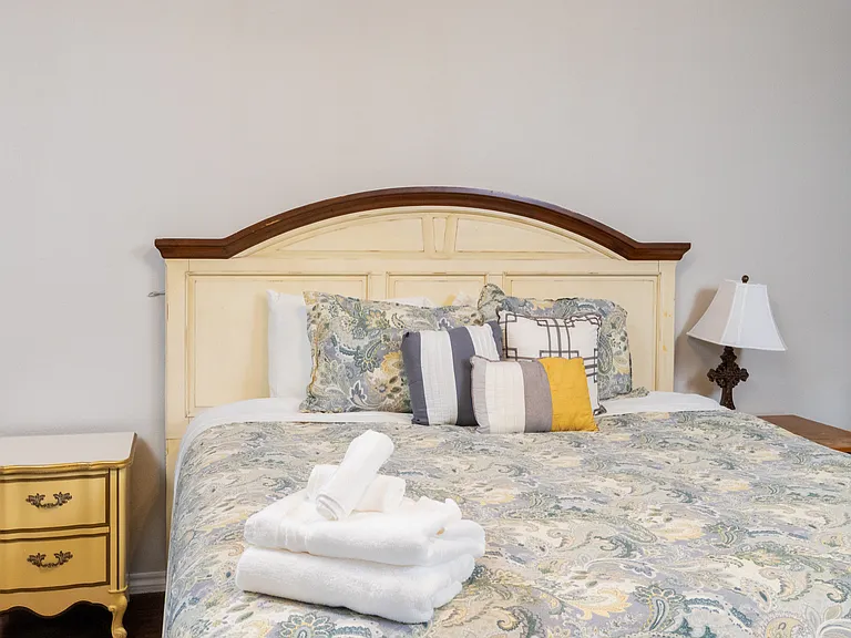 Relax in the primary bedroom with a king bed, soft bedding, TV, and warm lighting. Features a ceiling fan, dresser, room-darkening curtains, and a private attached bathroom for added comfort.