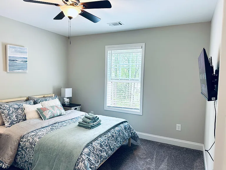 Furnished bedroom with ceiling fan, wall-mounted TV, and a large window with blinds for comfortable everyday living.