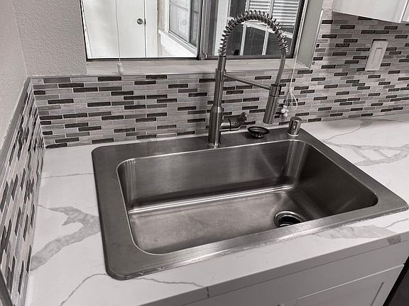 Large stainless steel sink with pull down faucet surrounded by beautiful quartz countertop.