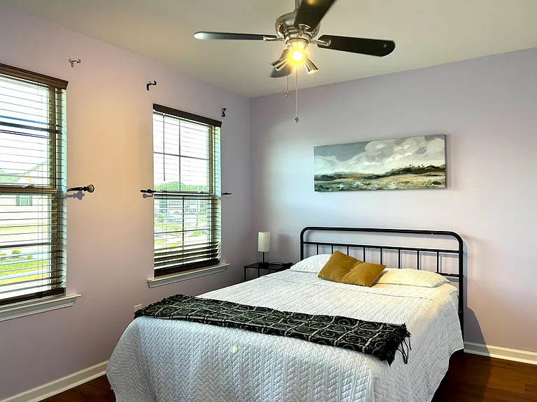 Well-sized bedroom with two windows, ceiling fan, and space for a full/queen bed plus a nightstand.