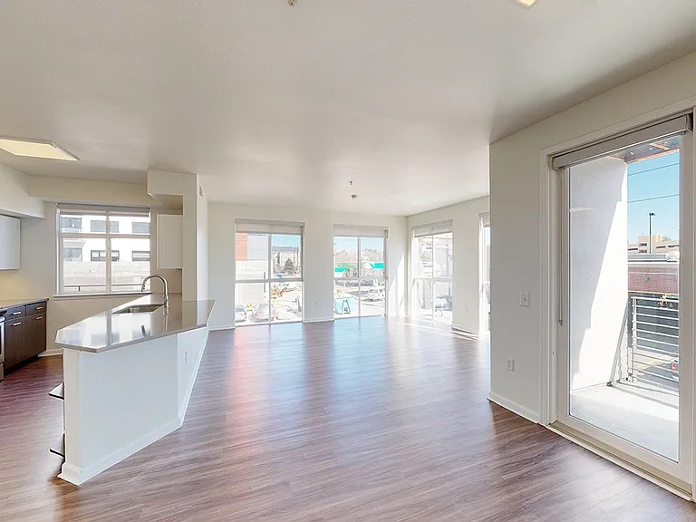 Apartment kitchen with stainless steel appliances, dining and living room with wood-style flooring.