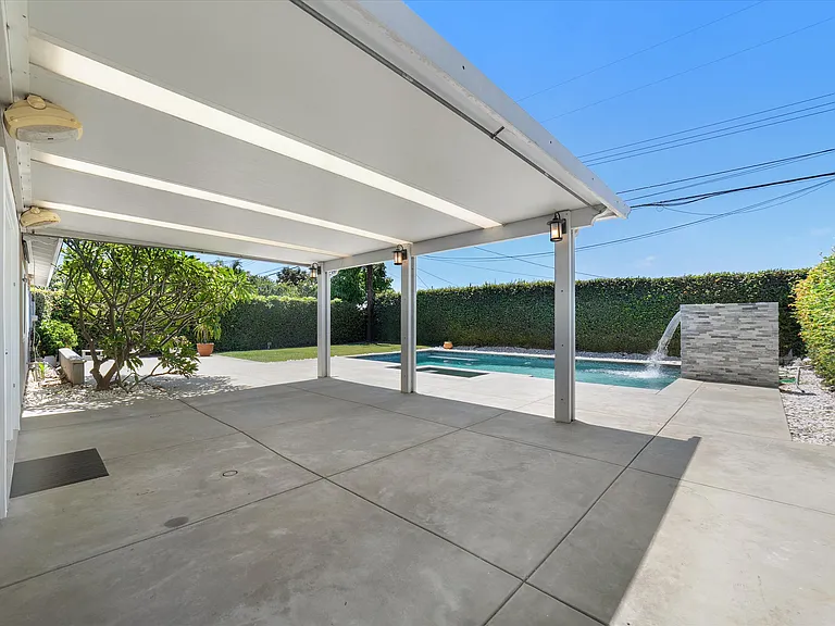 Looking out from house to backyard pool, dining area, hedges