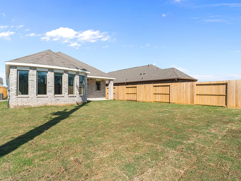 Rear view showcasing the signature bow window of the primary suite, four-sides brick construction, and spacious fenced backyard.
