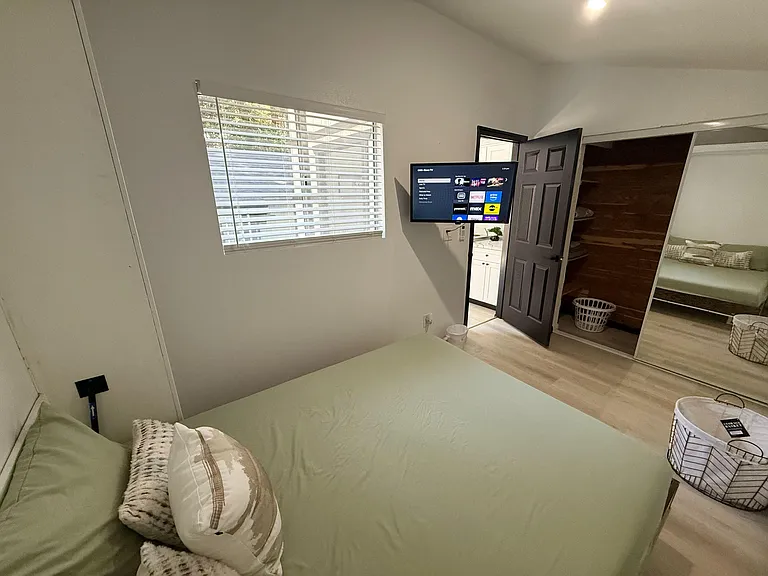 Bedroom with a large window, wall-mounted TV, and mirrored wardrobe with built-in shelving for storage.