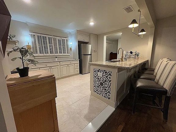 Kitchen featuring a kitchen breakfast bar, light stone counters, pendant lighting, freestanding refrigerator, and a peninsula