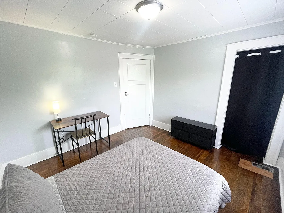 Furnished bedroom with wood-style flooring, a work desk, dresser storage, and a window with blackout covering. - N Gladstone Ave