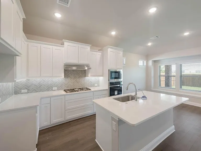 Modern kitchen featuring white cabinetry, a herringbone tile backsplash, white countertops, built-in stainless steel appliances, and a central island with an undermount sink
