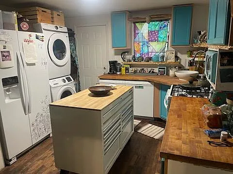 Compact kitchen featuring butcher-block counters, a center prep island, gas range, dishwasher, and in-unit stacked laundry.