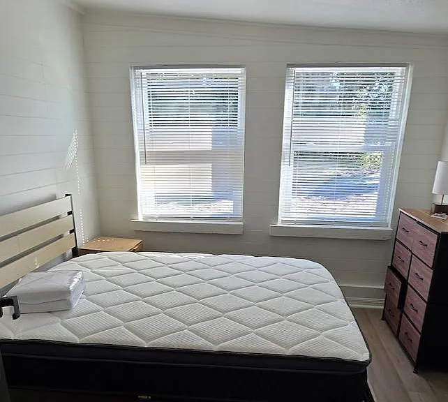 Furnished bedroom with a full bed, two windows with blinds, and a dresser for convenient everyday storage.