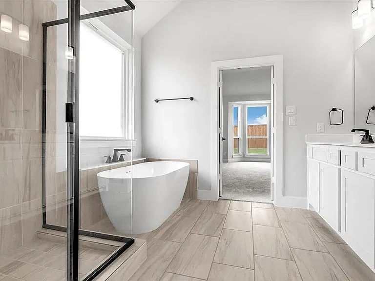 Bright bathroom featuring a freestanding tub, glass-enclosed shower, dual vanity with white cabinetry, and wood-finish tile flooring