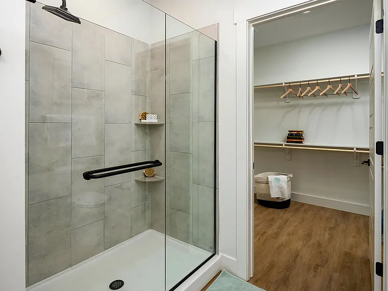 Bathroom features enclosed glass shower and open closet space with hangers and built-in shelving