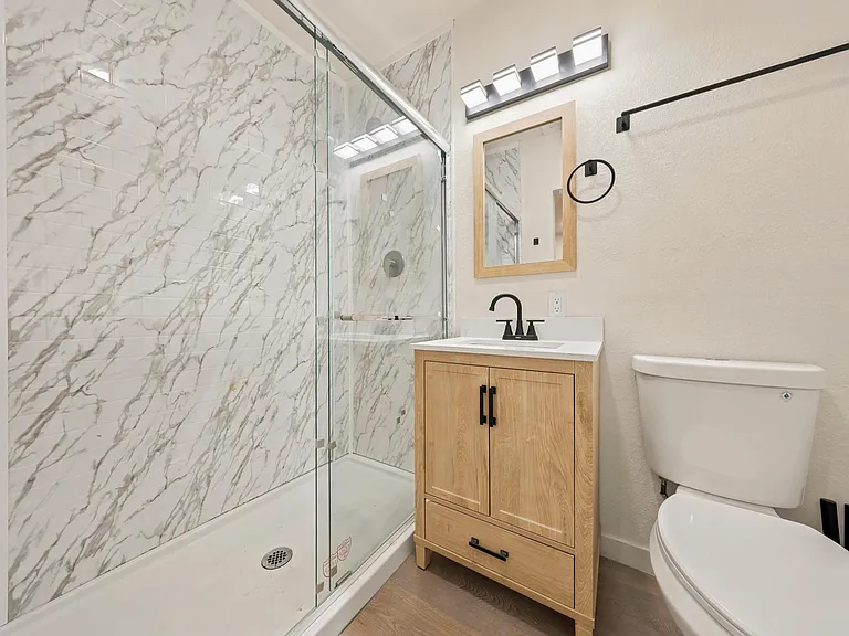 Updated bathroom with a glass-enclosed shower, marble-look tile surround, and a vanity with storage and modern lighting.
