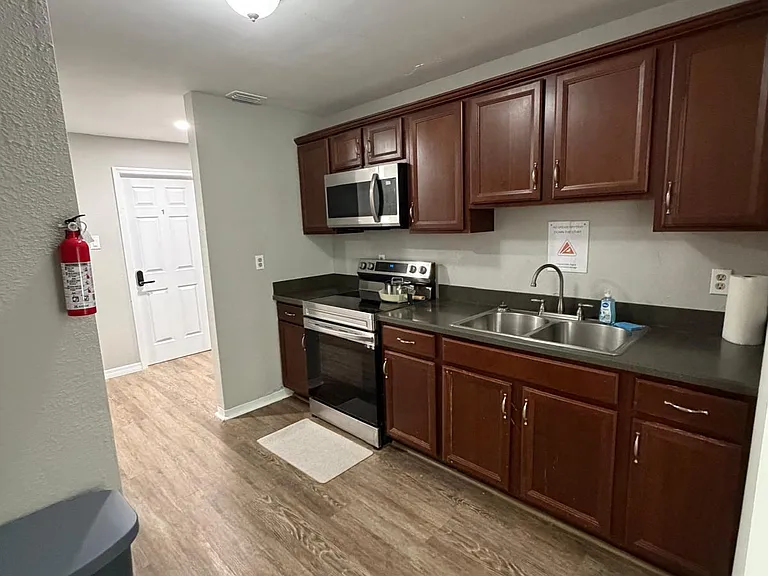 Efficient galley kitchen with ample wood cabinetry, laminate counters, double-basin sink, and stainless range and microwave.