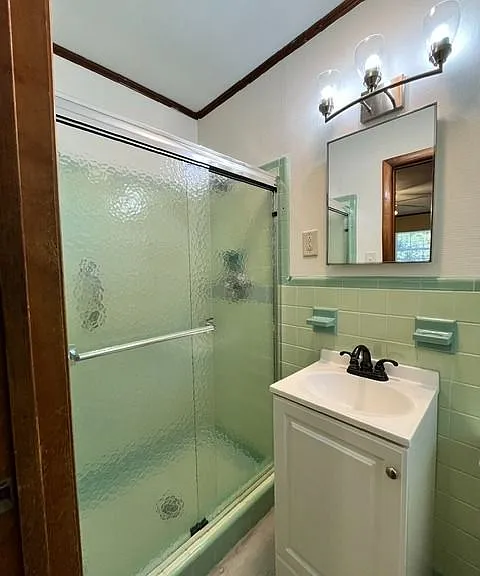 Updated bathroom with charming vintage character and modern touches throughout. Features include a spacious glass-enclosed shower combination, updated vanity with modern fixtures, stylish lighting, and durable flooring. The soft mint tile accents add uniq
