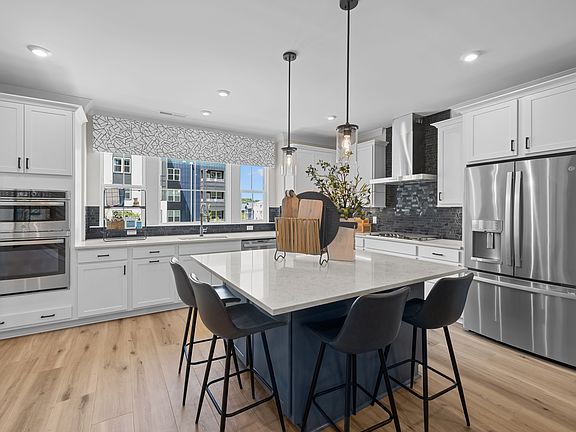 A modern, well-lit kitchen with white cabinets, a large island with bar stools, and stainless steel