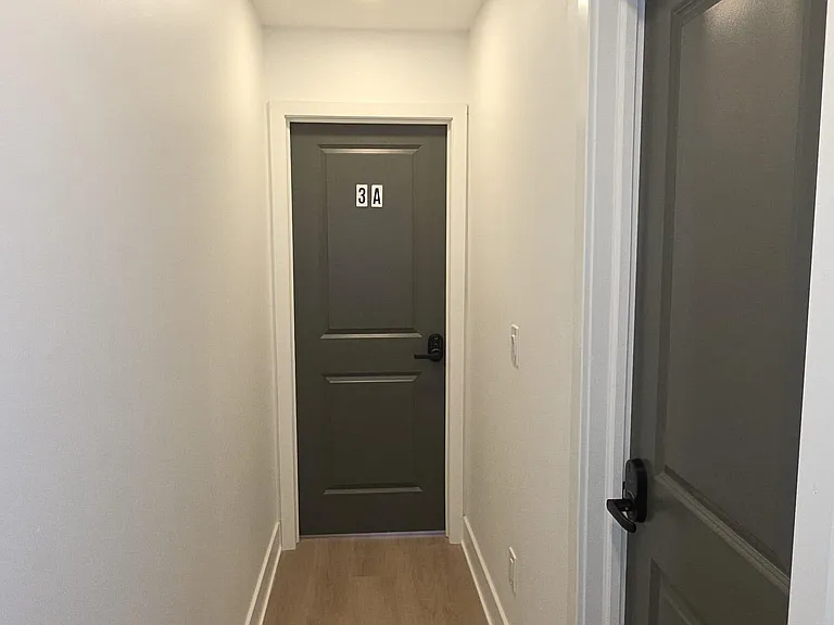 Clean interior hallway with durable wood-look flooring, recessed lighting, and multiple private doors for easy access.
