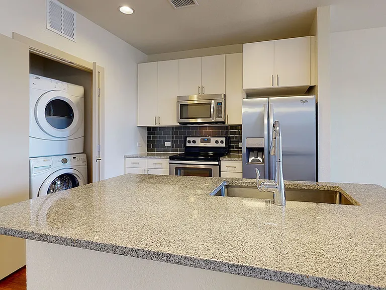 Apartment kitchen with stainless steel appliances, granite countertops and wood-style flooring.