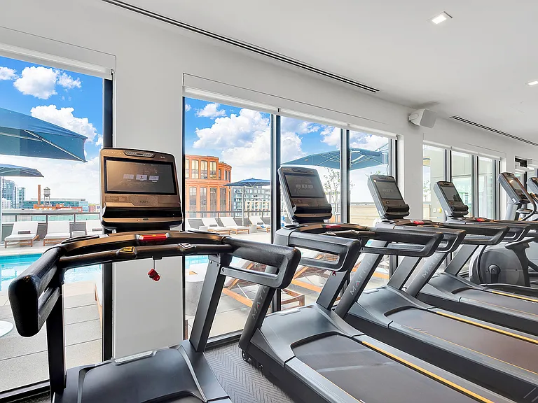 Modern gym with top-of-the-line treadmills and panoramic views of the city skyline and outdoor pool area.